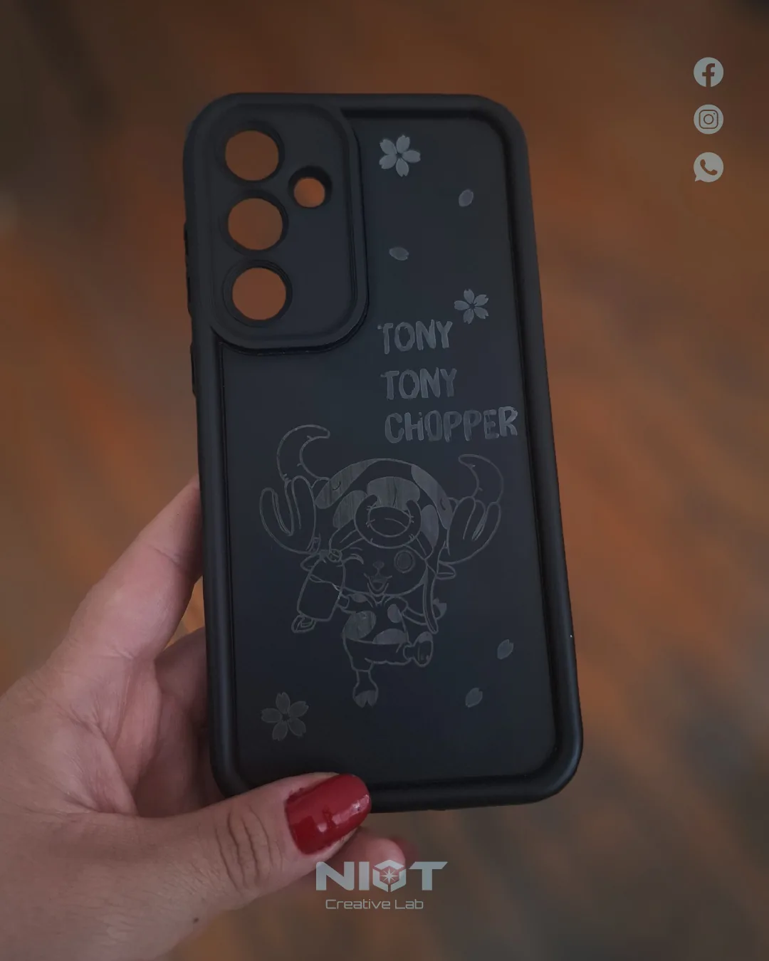 Funda negra de teléfono con grabado láser de Tony Tony Chopper y flores de cerezo, sostenida en mano.