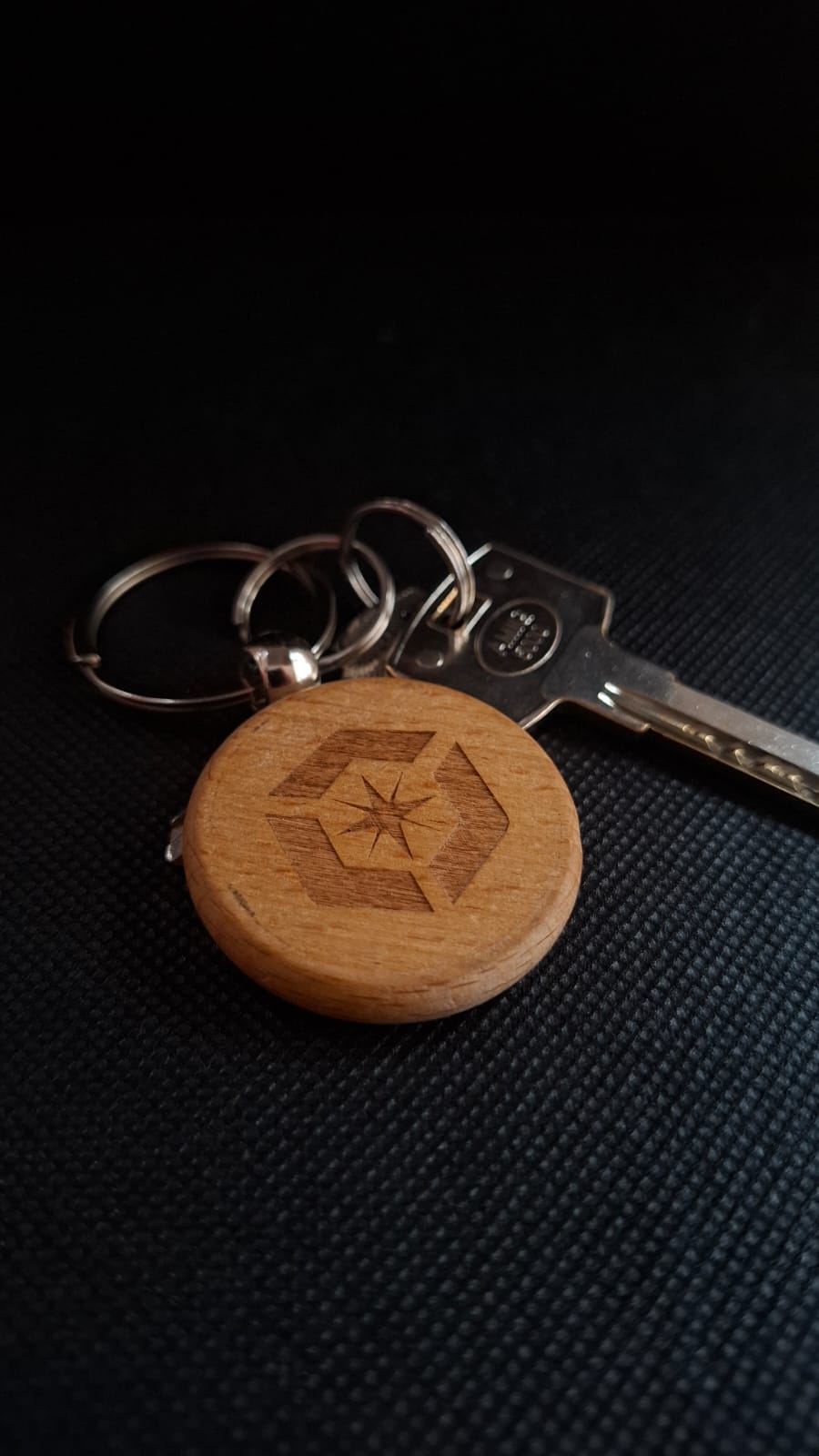 Llavero de madera con logo NIOT grabado por láser, sobre fondo oscuro.