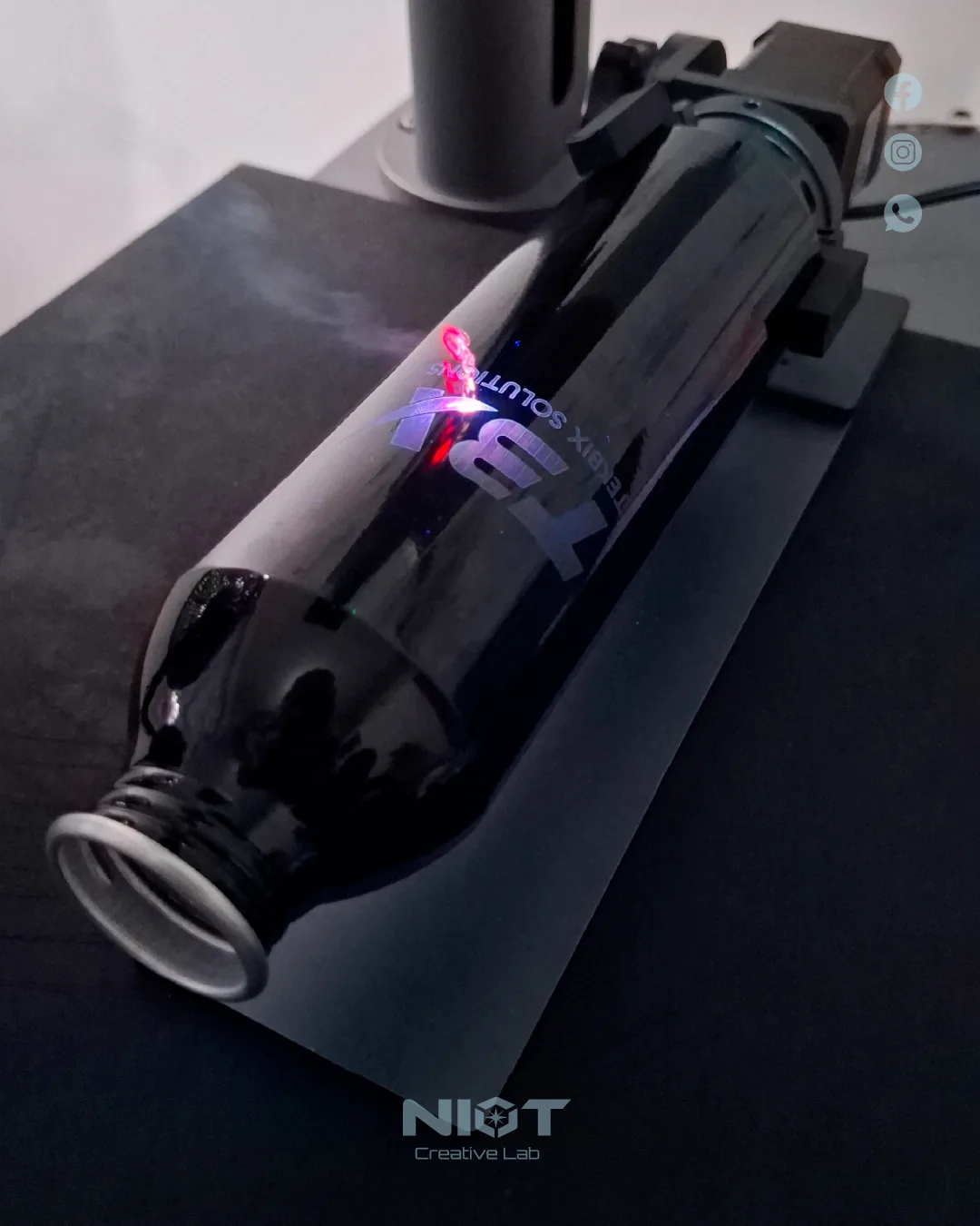Botella negra siendo grabada por el láser UV de NIOT con el haz rojo encendido sobre la superficie reflectiva.